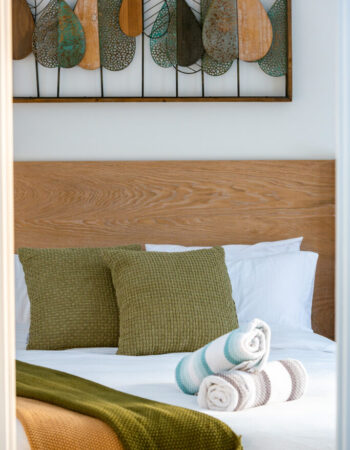 Queen bed with throw pillows and wooden head board. Metalic leaf artwork on the wall above.